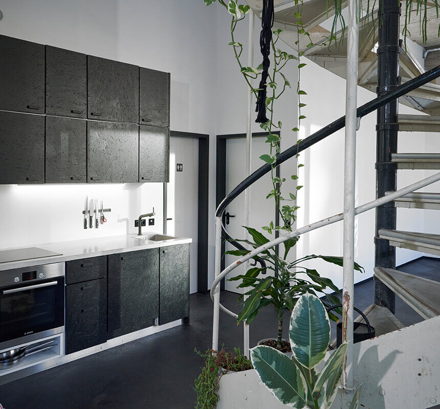 Minimalist kitchen with black cabinets, built-in oven, and visible spiral staircase at raw studios.