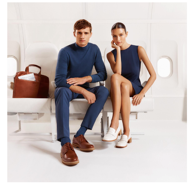 A striking campaign image featuring a handsome male and a beautiful female, both Caucasian, in a bright, white inflight setting, showcasing Lloyd shoes elegantly adorning their feet.