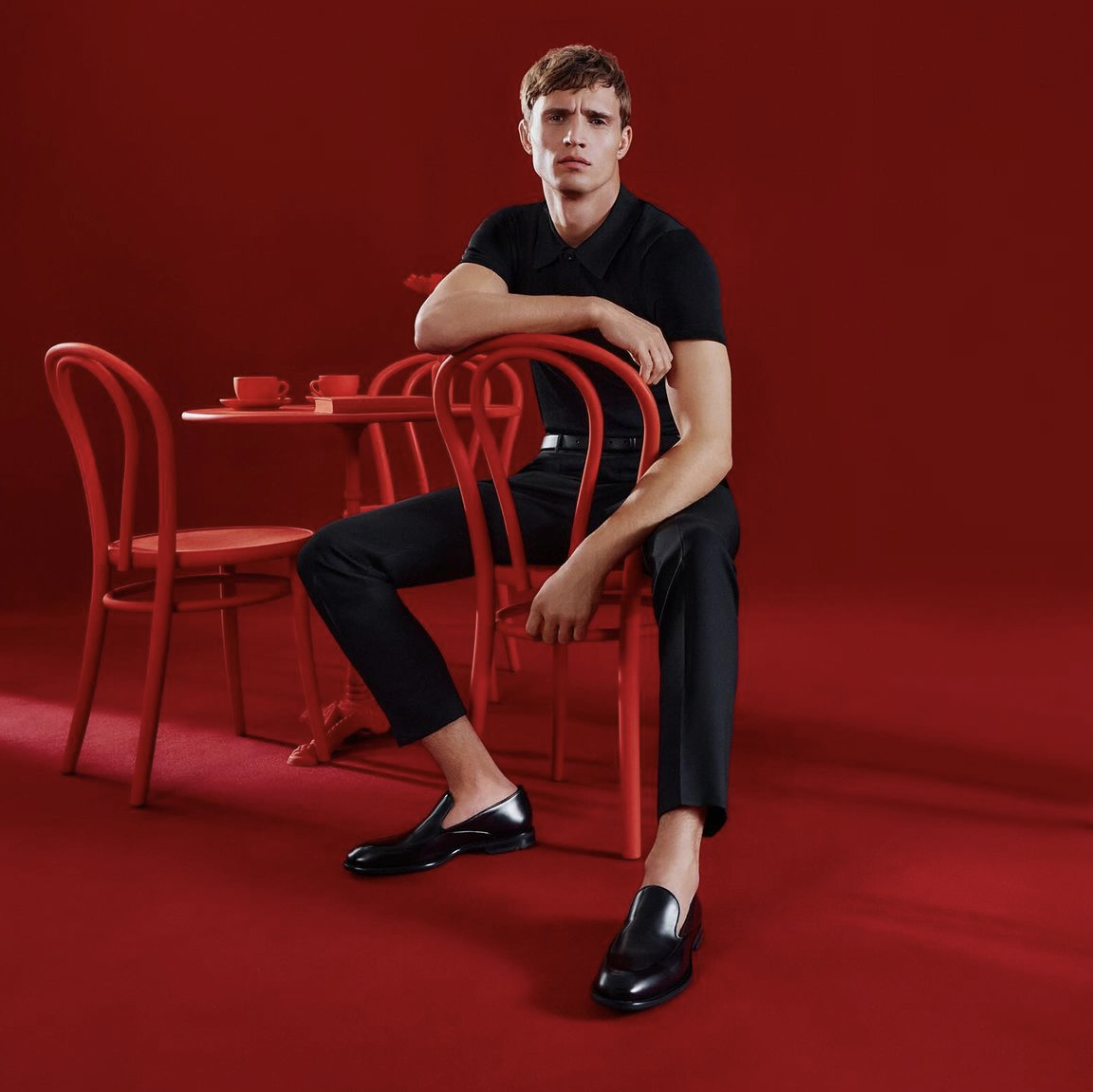 A striking image showcasing a Caucasian male model for the Lloyd Shoes SS24 campaign against a stylish all-red backdrop, including a red table, red chair, and red room décor.