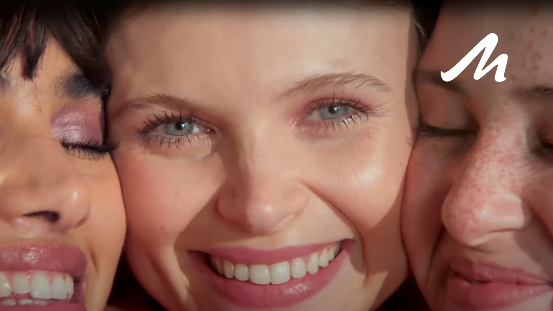 Three women—Sarah Carstens, Dulcie, and Marisabelle—pose cheek-to-cheek with radiant smiles, showcasing Manhattan Eyemazing Mascara.