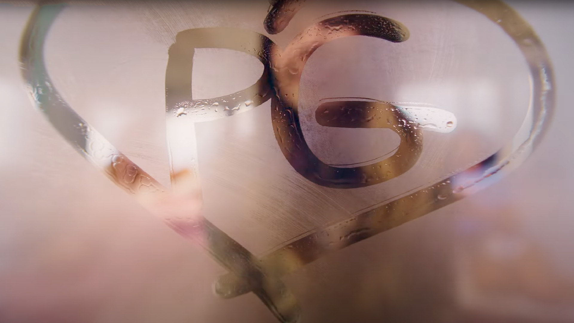 A heart shape is drawn on a fogged-up glass surface with the letters "PG" written inside. The condensation and soft reflections create a dreamy, intimate atmosphere, hinting at the theme of the music video.