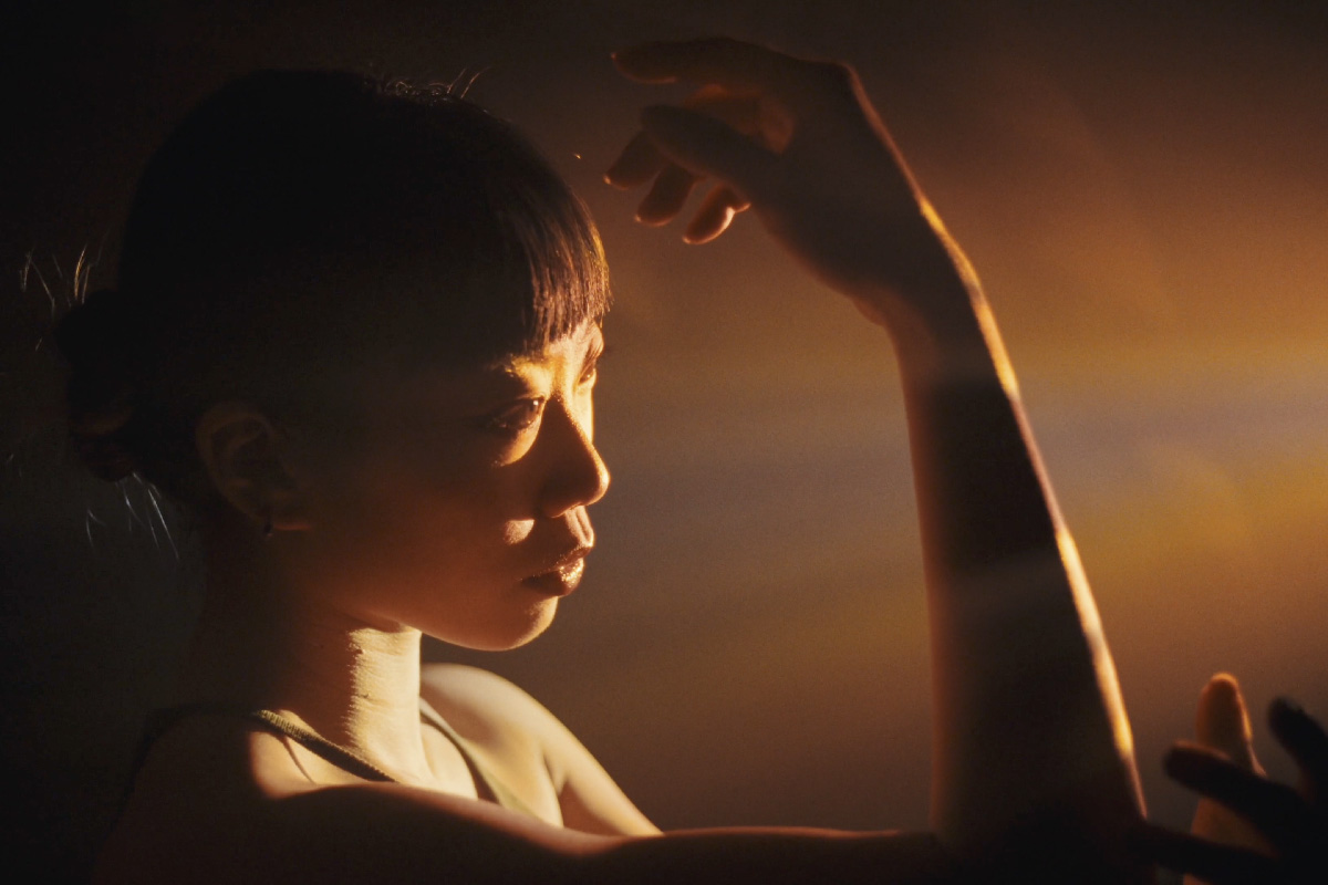 Close-up of a performer (@dori.moves) gracefully illuminated by cinematic lighting, highlighting their hand and face in a warm, moody ambiance.