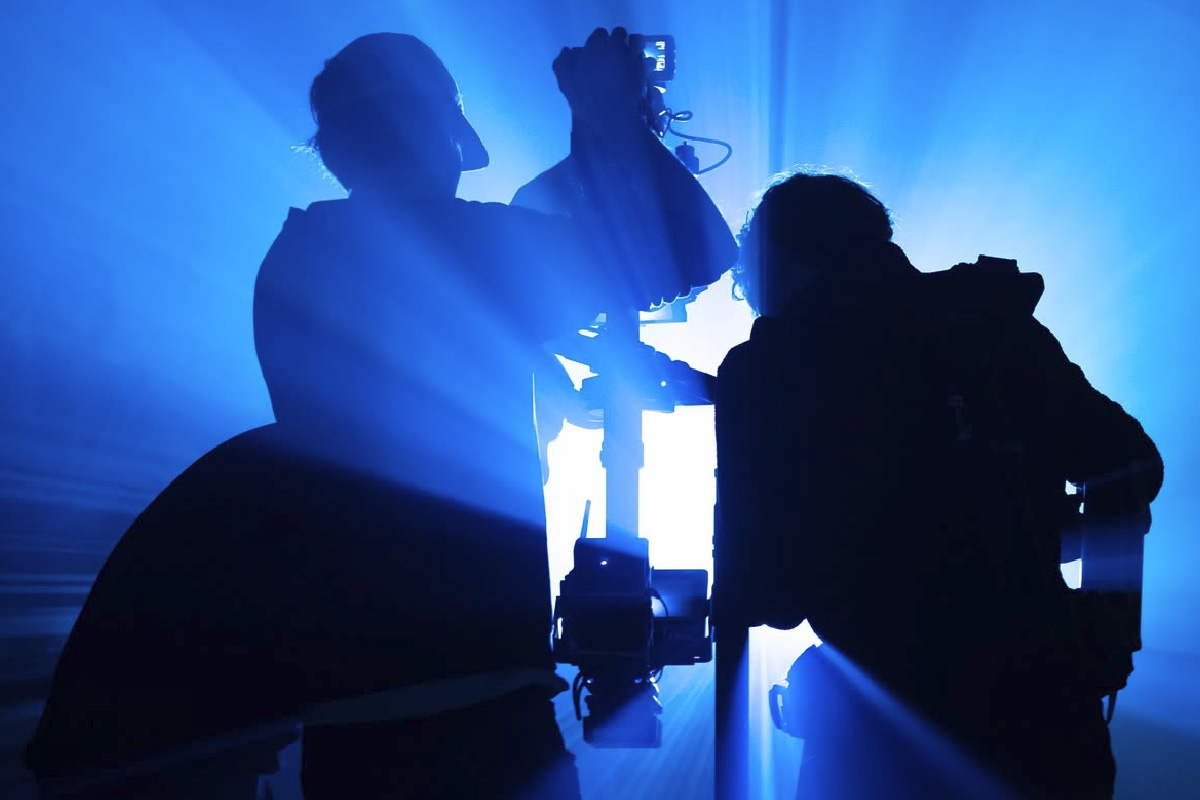 Silhouettes of two camera operators working together in dramatic blue lighting, creating a cinematic effect.