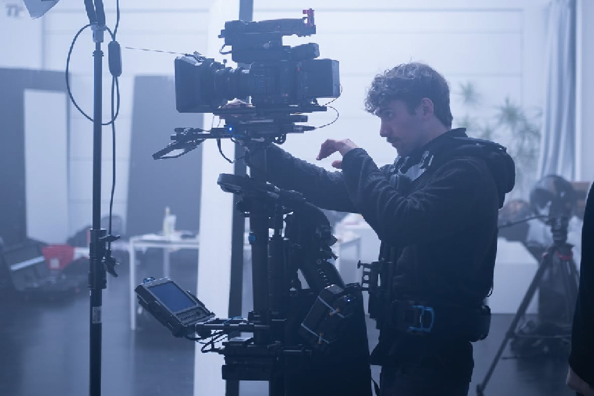 A focused camera operator adjusting a large cinema camera rig in a professional studio setting, with a softly lit background.