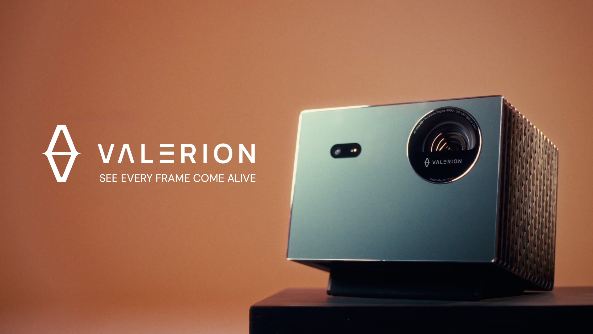 The Valerion VisionMaster Max home cinema projector on a pedestal, presented with the brand logo and tagline 'See Every Frame Come Alive' against a sleek, warm background.