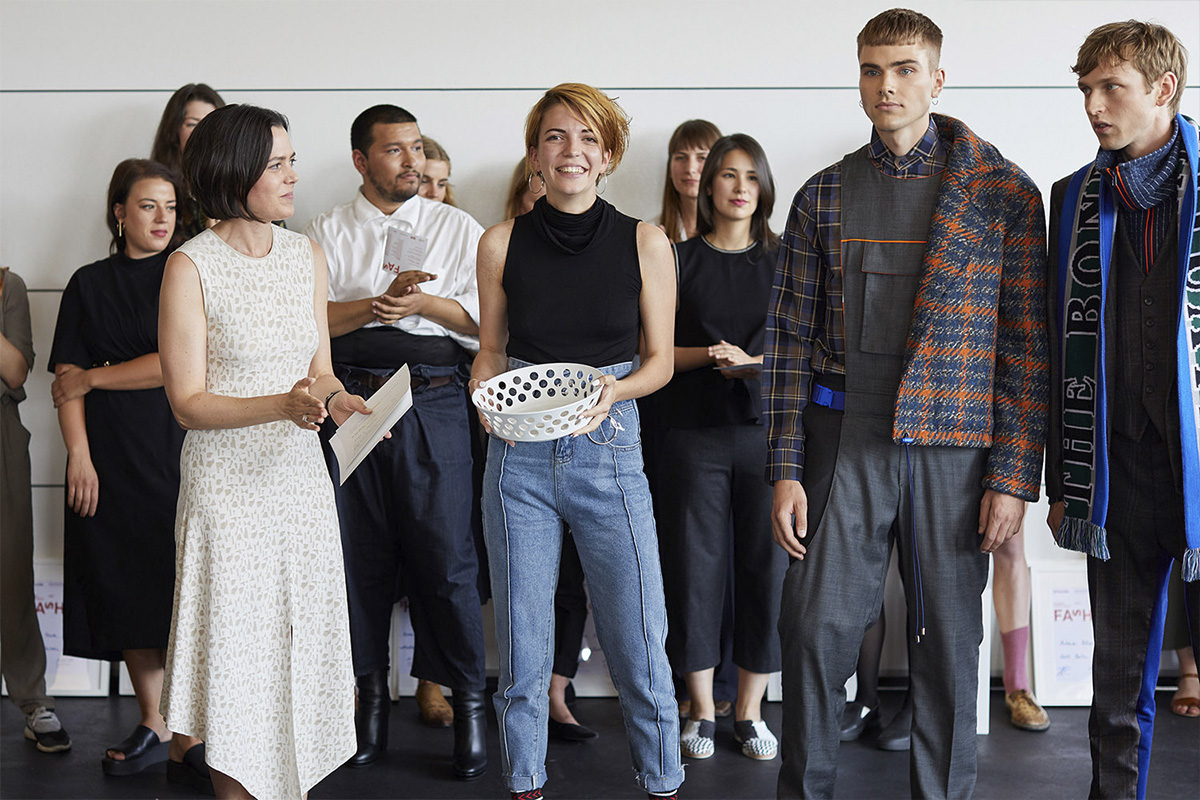 A moment from the FASH Award 2018 ceremony at raw studios., featuring a smiling winner holding a white sculptural bowl award.