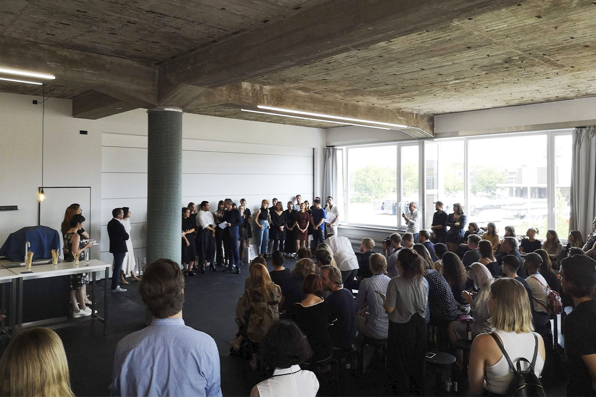 A wide shot of the FASH Award 2018 event at raw studios., capturing an audience gathered in a sunlit, industrial-style space as designers and models prepare for the announcement.