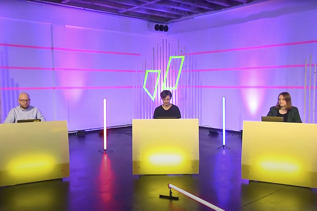 Three speakers sit behind illuminated yellow podiums in a futuristic stage setup at raw studios. Neon geometric designs and vertical LED lighting create a visually engaging environment for the Junge Liberale Buko62 event.