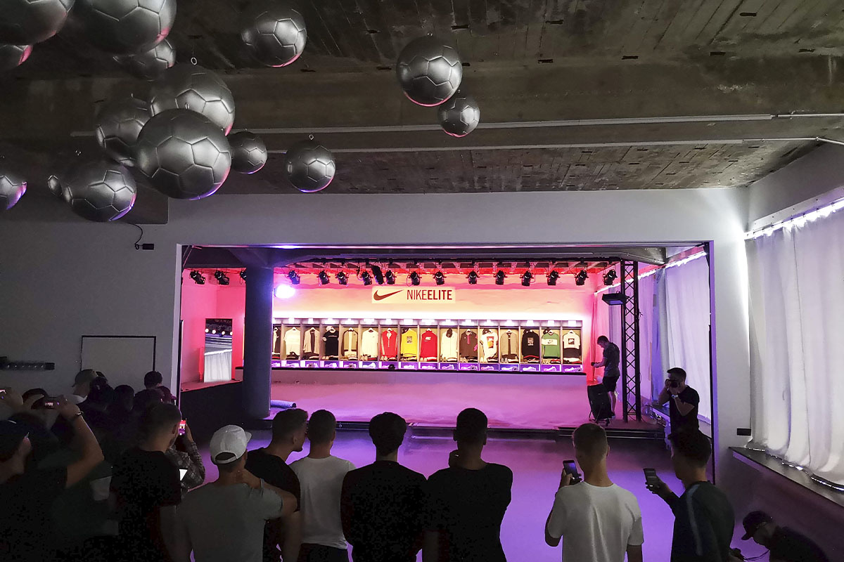 A group of young soccer players gathers at raw studios., watching an illuminated display of Nike’s latest soccer jerseys and apparel. Overhead, silver soccer ball decorations add to the event’s immersive atmosphere.