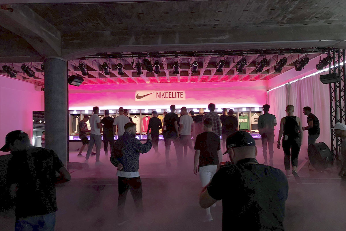 Attendees walk toward the Nike ELITE display at raw studios., which is bathed in dramatic red and purple lighting.