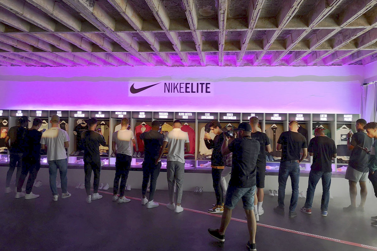 A close-up of the Nike ELITE locker-style display, featuring individual sections showcasing the latest soccer jerseys, shoes, and gear. Attendees examine the details, taking photos and engaging with the products.