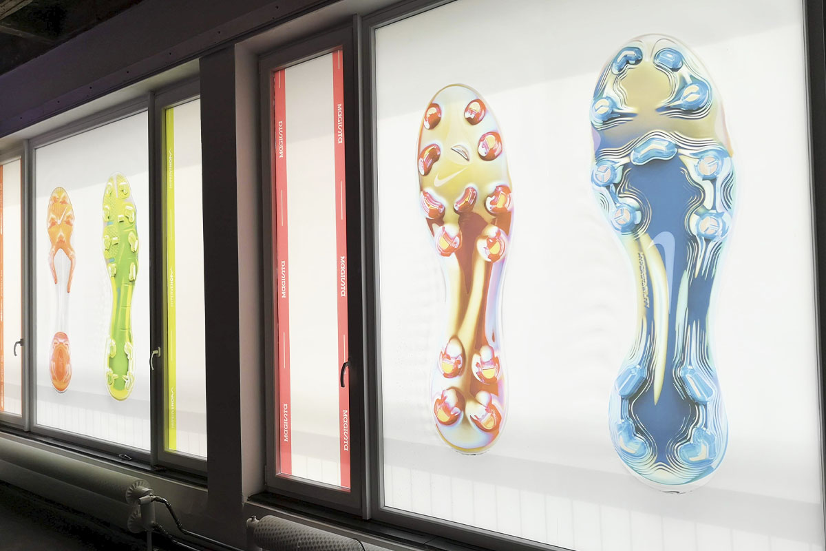 A futuristic window display featuring large, illuminated images of Nike soccer cleats in various colors and designs. The vibrant visuals highlight the innovation in Nike’s latest footwear technology.