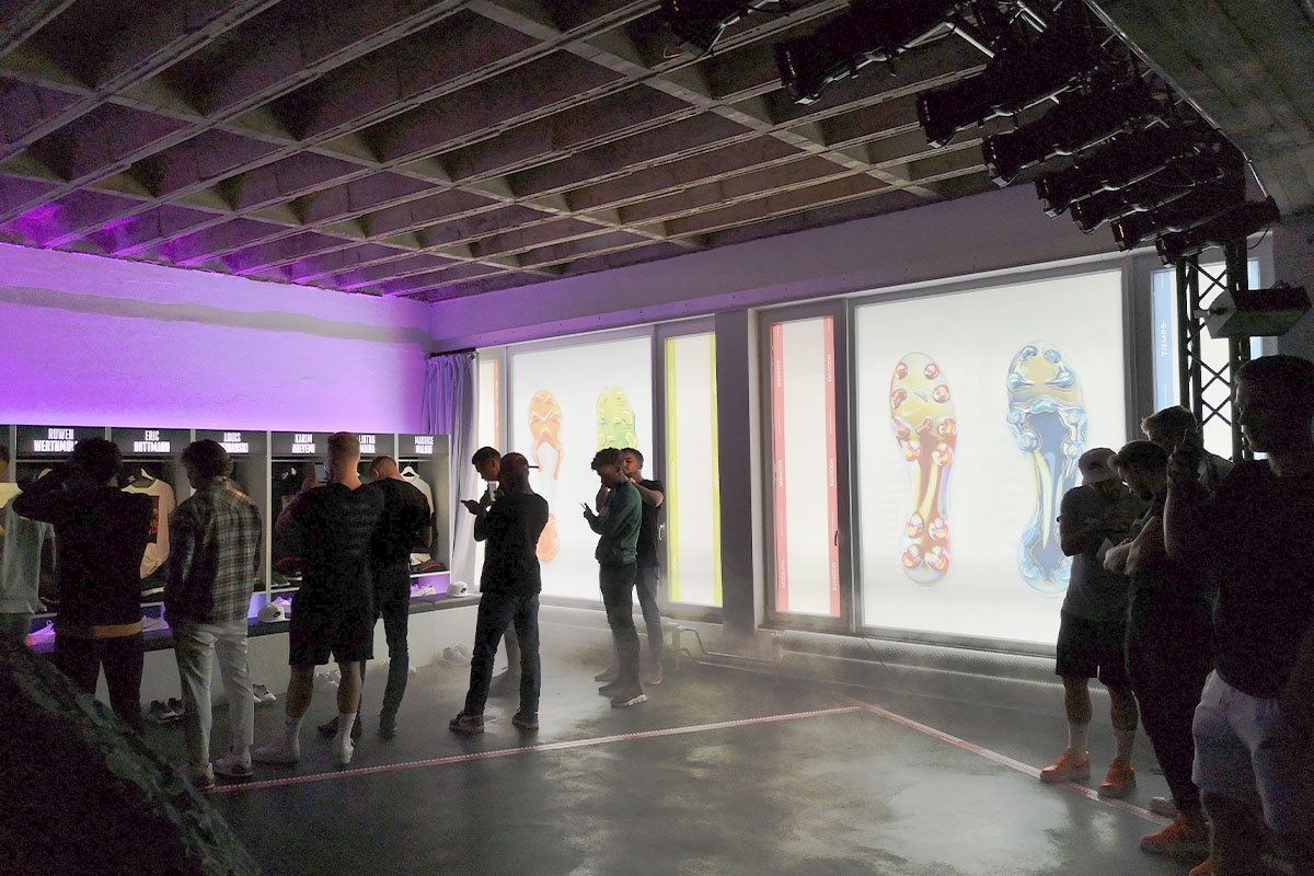 A group of young soccer players interacts with the Nike ELITE collection at raw studios., standing in front of the product display while the event’s atmospheric lighting and fog effects create an immersive experience.