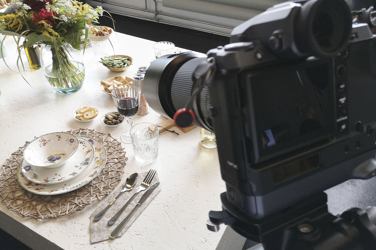 A close-up of a professional Fujifilm camera capturing a beautifully set dining table with plates, glasses, and fresh food, showcasing the camera’s capabilities at the Fuji Road Show.