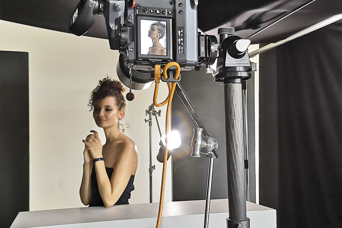 A model posing in a controlled studio lighting setup, viewed through the screen of a Fujifilm camera, demonstrating portrait photography techniques at the Fuji Road Show at raw studios.