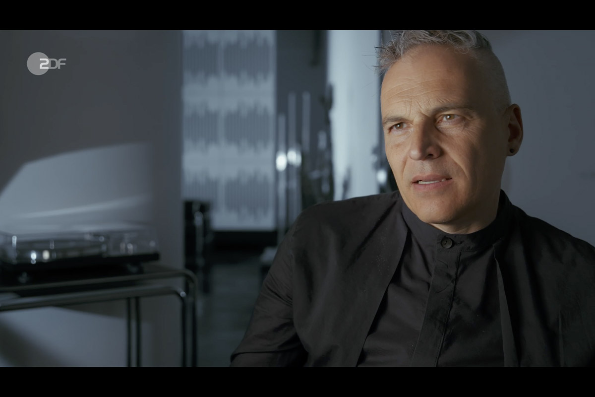 Interview shot of Gerhard Schick, seated in a modern studio environment, appearing thoughtful during filming for the Cum-Ex documentary.