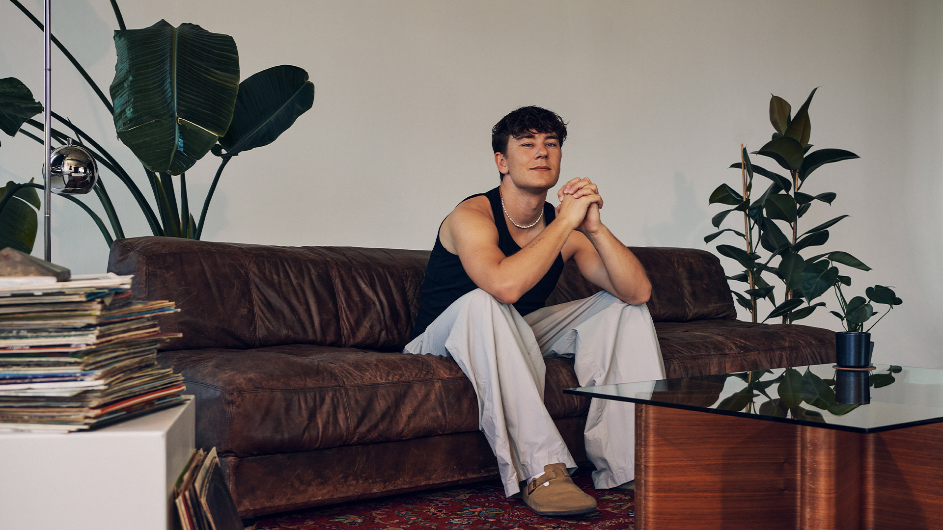 German DJ and artist BUNT. relaxing on a vintage leather sofa at raw studios, a rental studios berlin location, with vinyl records and indoor plants creating a cozy, creative photoshoot studio berlin vibe.